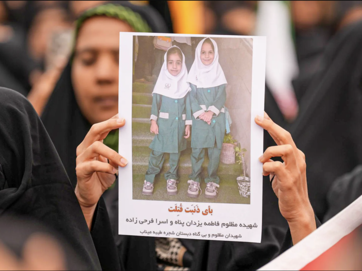 Photo of two school girls wearing white headscarfs, green uniforms, and sneakers